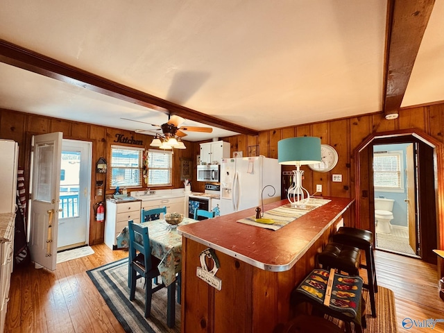 kitchen with beamed ceiling, light wood finished floors, stainless steel microwave, white fridge with ice dispenser, and range with electric cooktop