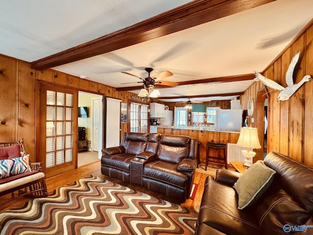 living room with light wood-type flooring, beamed ceiling, ceiling fan, and wooden walls