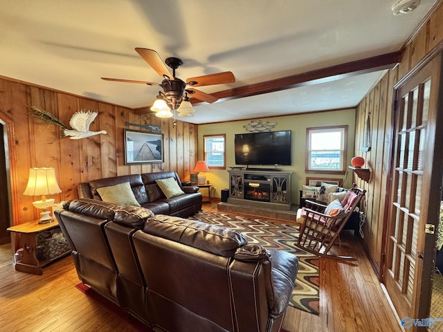 living room with wooden walls, a ceiling fan, a glass covered fireplace, and hardwood / wood-style floors