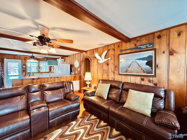 living area featuring beamed ceiling, wooden walls, wood finished floors, and ceiling fan