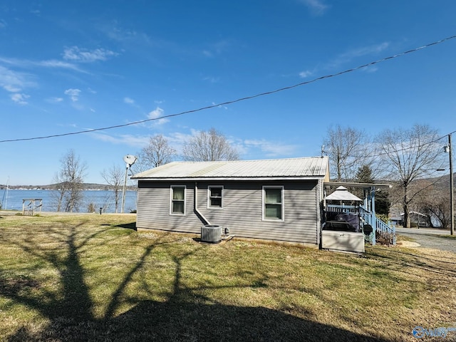rear view of property with a lawn, metal roof, cooling unit, and a water view