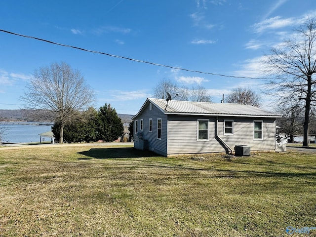 view of property exterior with a water view, central air condition unit, a yard, and metal roof