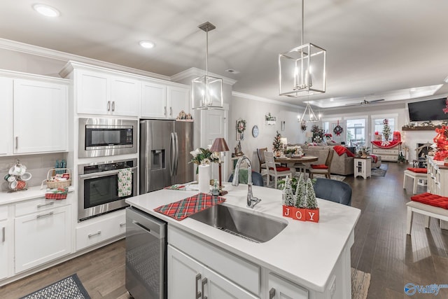 kitchen with stainless steel appliances, sink, decorative light fixtures, white cabinetry, and an island with sink