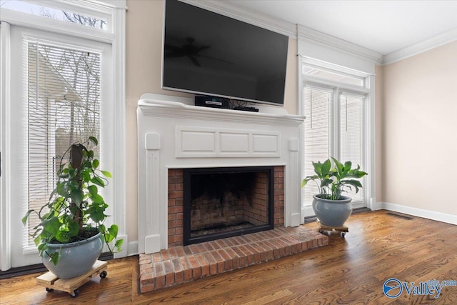 living area featuring visible vents, ornamental molding, a brick fireplace, wood finished floors, and baseboards