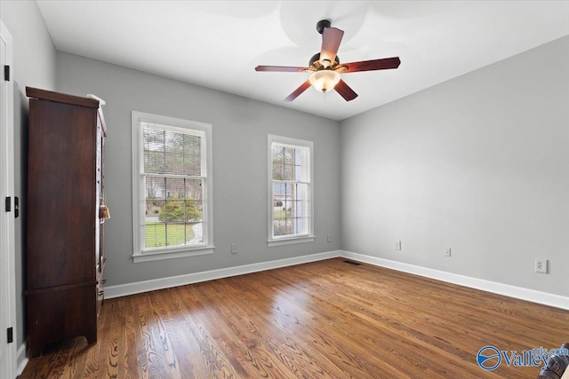 unfurnished room featuring visible vents, wood finished floors, a ceiling fan, and baseboards