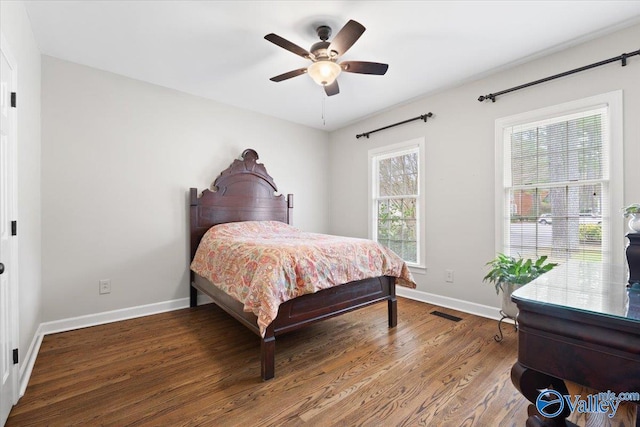 bedroom with a ceiling fan, visible vents, baseboards, and wood finished floors