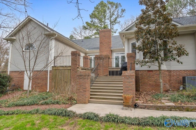 view of front of house featuring brick siding, roof with shingles, a chimney, central air condition unit, and stairway