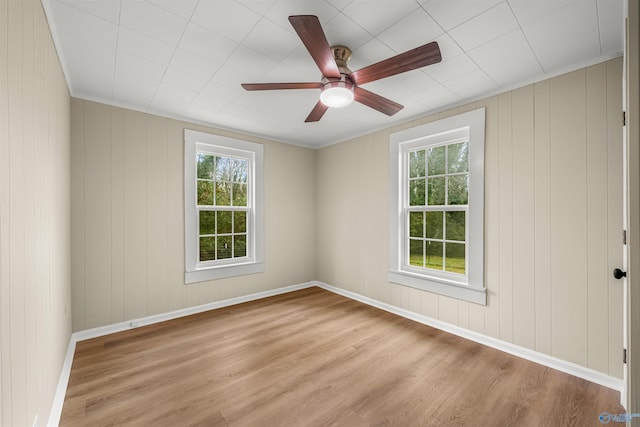 unfurnished room with ceiling fan, light hardwood / wood-style flooring, crown molding, and wooden walls