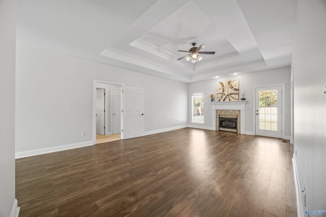 unfurnished living room with a tiled fireplace, a tray ceiling, dark hardwood / wood-style floors, and ceiling fan