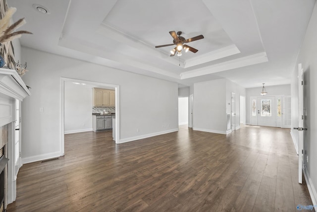 unfurnished living room with crown molding, a tray ceiling, dark wood-type flooring, and ceiling fan