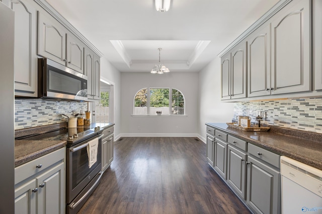 kitchen with a tray ceiling, stainless steel appliances, gray cabinets, a chandelier, and dark hardwood / wood-style floors