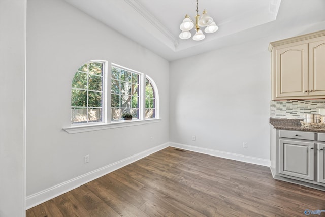 unfurnished dining area featuring a notable chandelier, ornamental molding, dark wood-type flooring, and a raised ceiling