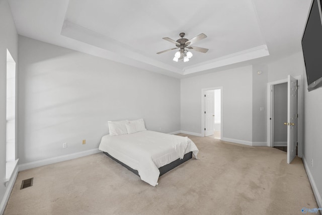 bedroom featuring connected bathroom, light colored carpet, a tray ceiling, and ceiling fan