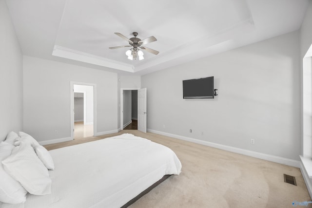 bedroom with a spacious closet, ceiling fan, a raised ceiling, and light carpet