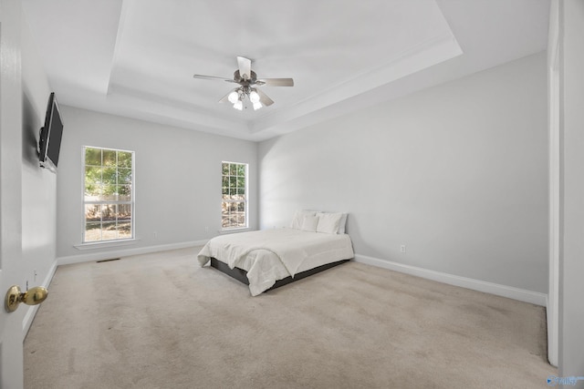 bedroom featuring a raised ceiling, light colored carpet, and ceiling fan