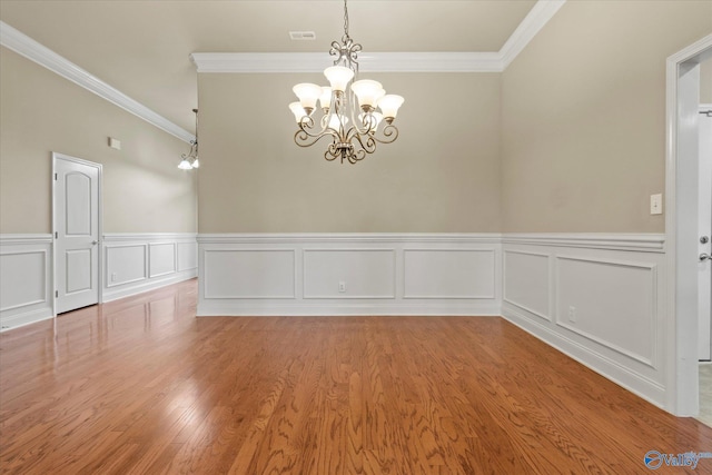 unfurnished room with hardwood / wood-style flooring, ornamental molding, and a notable chandelier