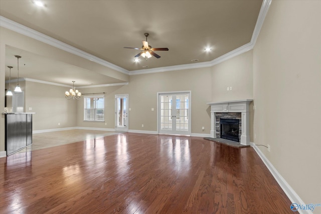 unfurnished living room featuring french doors, ornamental molding, ceiling fan with notable chandelier, wood-type flooring, and a stone fireplace