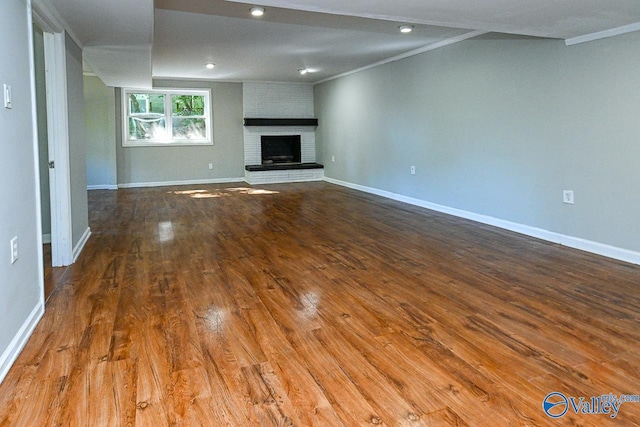 unfurnished living room featuring hardwood / wood-style flooring, crown molding, and a brick fireplace