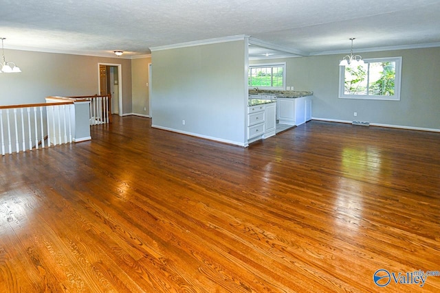 unfurnished living room with wood-type flooring, ornamental molding, a chandelier, and a textured ceiling