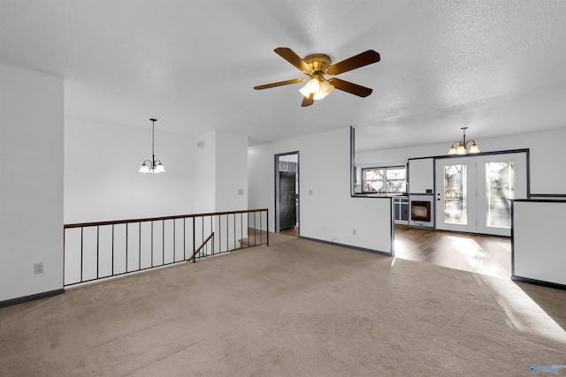 unfurnished living room featuring a textured ceiling, carpet floors, and ceiling fan with notable chandelier