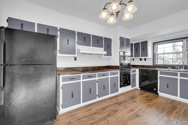 kitchen with hardwood / wood-style flooring, an inviting chandelier, black appliances, and sink