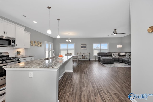 kitchen with stainless steel appliances, a center island with sink, white cabinetry, ceiling fan with notable chandelier, and sink