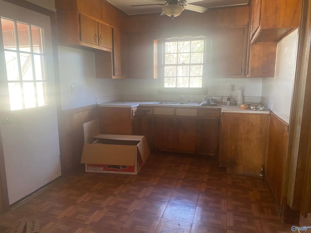 kitchen with wainscoting, a sink, a ceiling fan, and brown cabinets