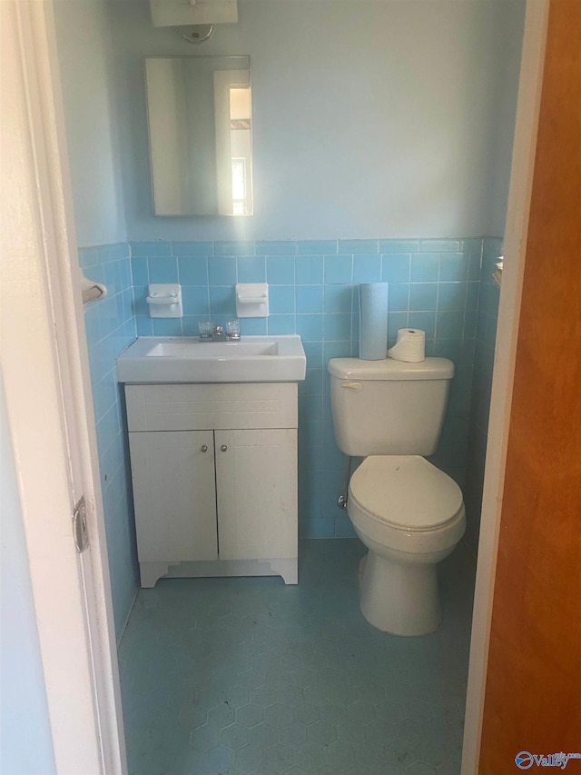 bathroom featuring toilet, a wainscoted wall, tile walls, and vanity