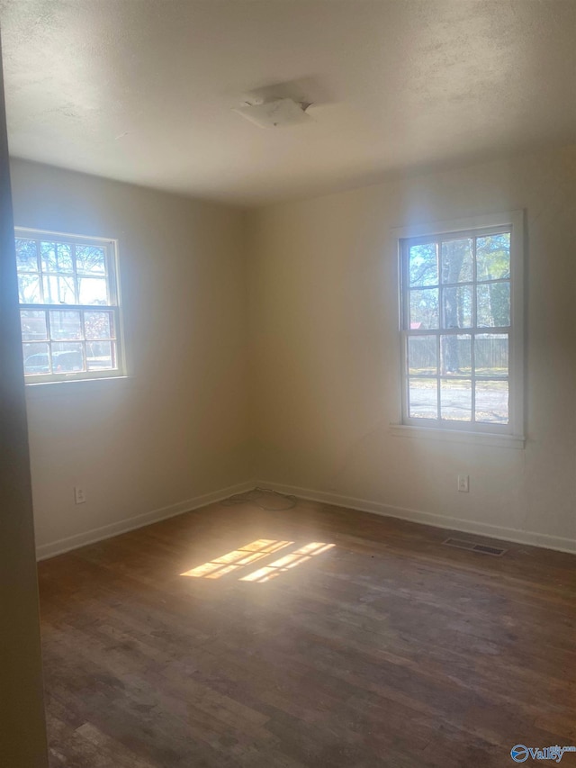 empty room featuring plenty of natural light, visible vents, baseboards, and dark wood-type flooring