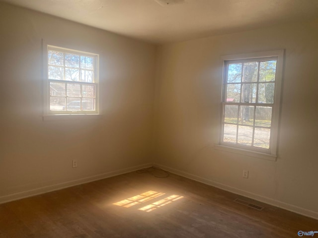 unfurnished room with baseboards, wood finished floors, visible vents, and a healthy amount of sunlight