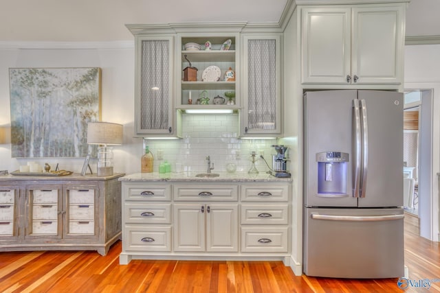 bar featuring stainless steel refrigerator with ice dispenser, decorative backsplash, ornamental molding, light stone counters, and sink