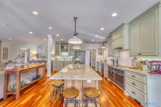 kitchen with light stone countertops, pendant lighting, appliances with stainless steel finishes, backsplash, and a center island with sink