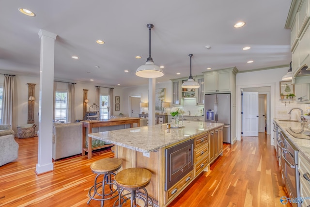 kitchen featuring ornate columns, stainless steel appliances, hanging light fixtures, a kitchen island, and light hardwood / wood-style flooring