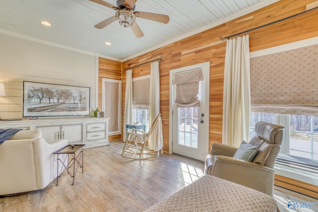 living room with ceiling fan, a wealth of natural light, wood walls, and crown molding