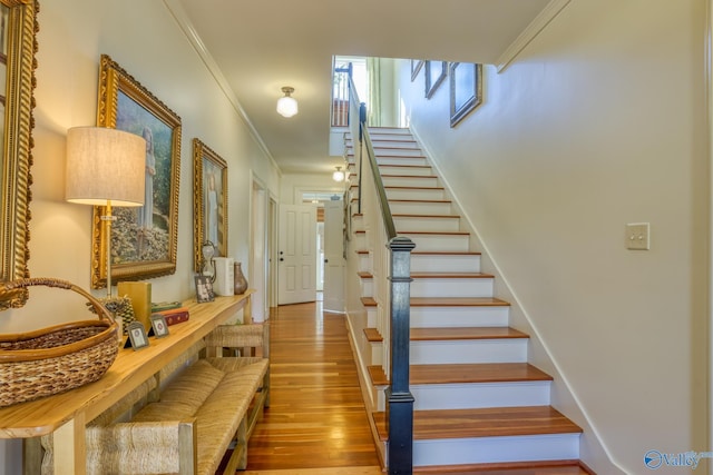 staircase with wood-type flooring and ornamental molding