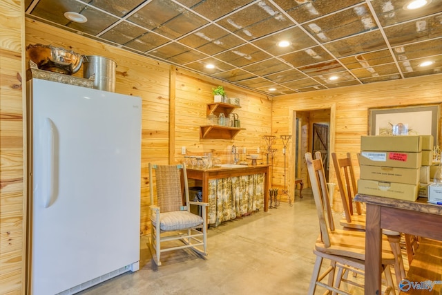 interior space with white refrigerator, wood walls, and concrete floors