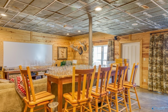 dining space with concrete flooring, bar, and wooden walls