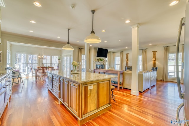 kitchen with decorative light fixtures, a notable chandelier, a center island, light wood-type flooring, and light stone counters