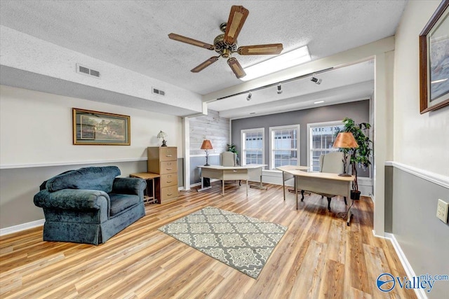 living area with visible vents, a textured ceiling, baseboards, and wood finished floors