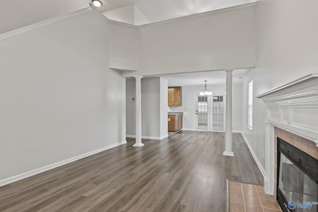 unfurnished living room with a tile fireplace, an inviting chandelier, crown molding, a towering ceiling, and dark hardwood / wood-style flooring