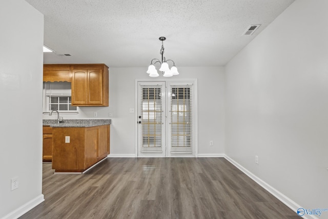 unfurnished dining area with a textured ceiling, dark hardwood / wood-style flooring, an inviting chandelier, and sink