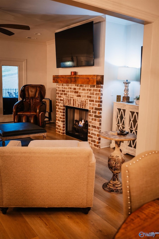 living area featuring a ceiling fan, a brick fireplace, wood finished floors, and crown molding