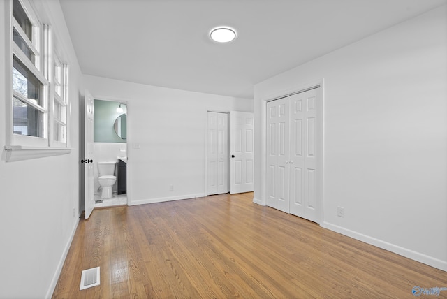 unfurnished bedroom featuring multiple closets, connected bathroom, and light hardwood / wood-style flooring