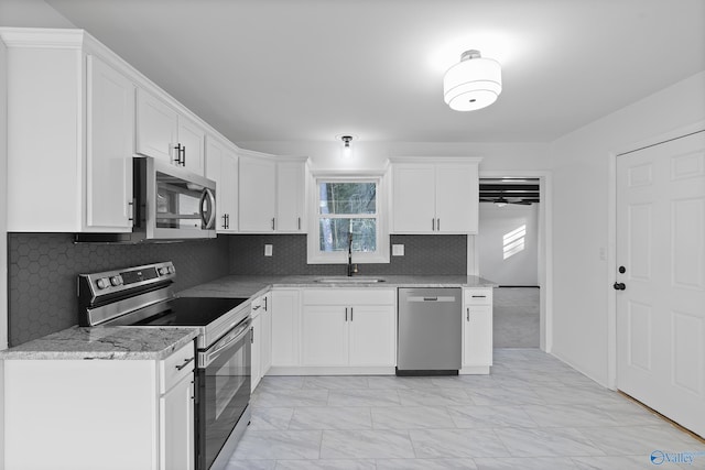 kitchen with light stone counters, a wealth of natural light, stainless steel appliances, sink, and white cabinets