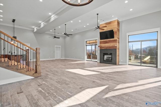 unfurnished living room with ceiling fan, a large fireplace, a towering ceiling, and light hardwood / wood-style flooring