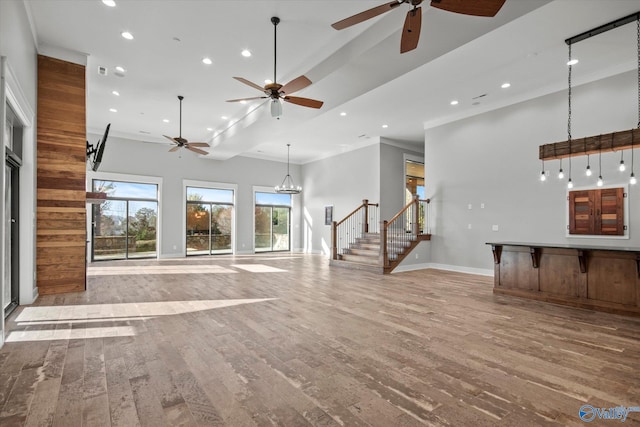 unfurnished living room with ceiling fan, light hardwood / wood-style floors, ornamental molding, and a high ceiling