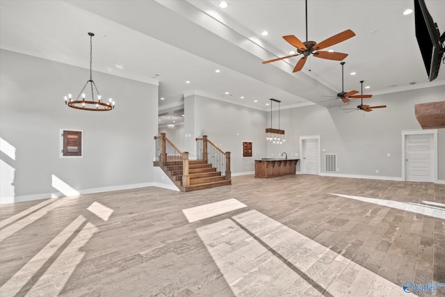 unfurnished living room with light hardwood / wood-style flooring, a high ceiling, and ceiling fan with notable chandelier