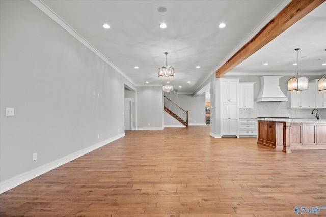 unfurnished living room featuring light hardwood / wood-style floors, sink, crown molding, and a chandelier