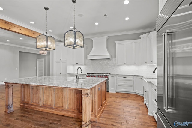 kitchen with light stone counters, custom exhaust hood, high end appliances, white cabinetry, and a large island