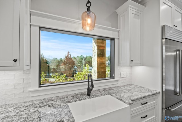 kitchen featuring white cabinets, hanging light fixtures, built in fridge, and sink